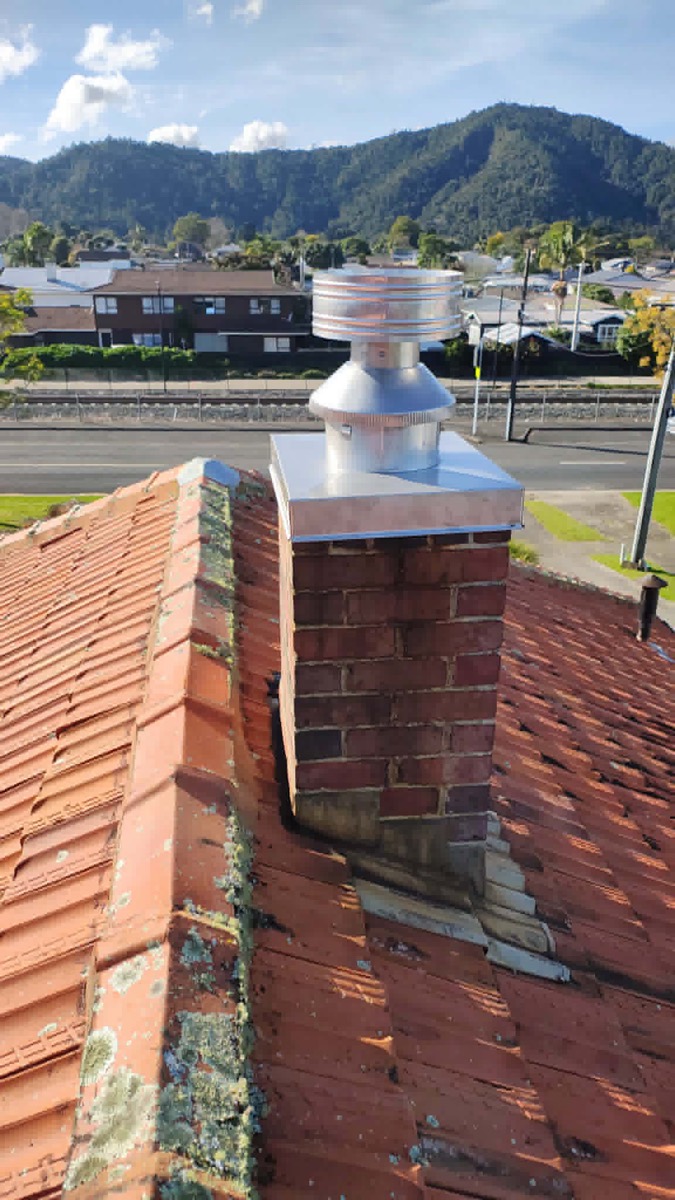 A new stainless steel cowl and flashing on the same brick chimney, tiled roof — after