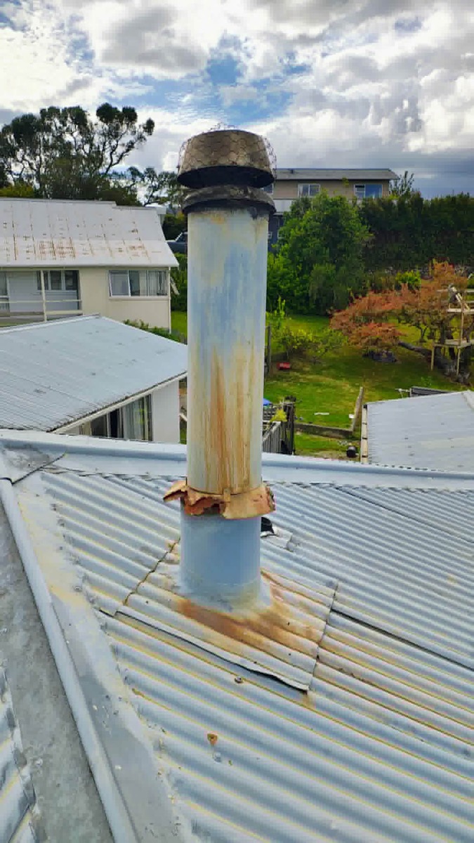A corroded, rusty old flue pipe and cap on a corrugated metal roof — before Premium Fires re-flued it
