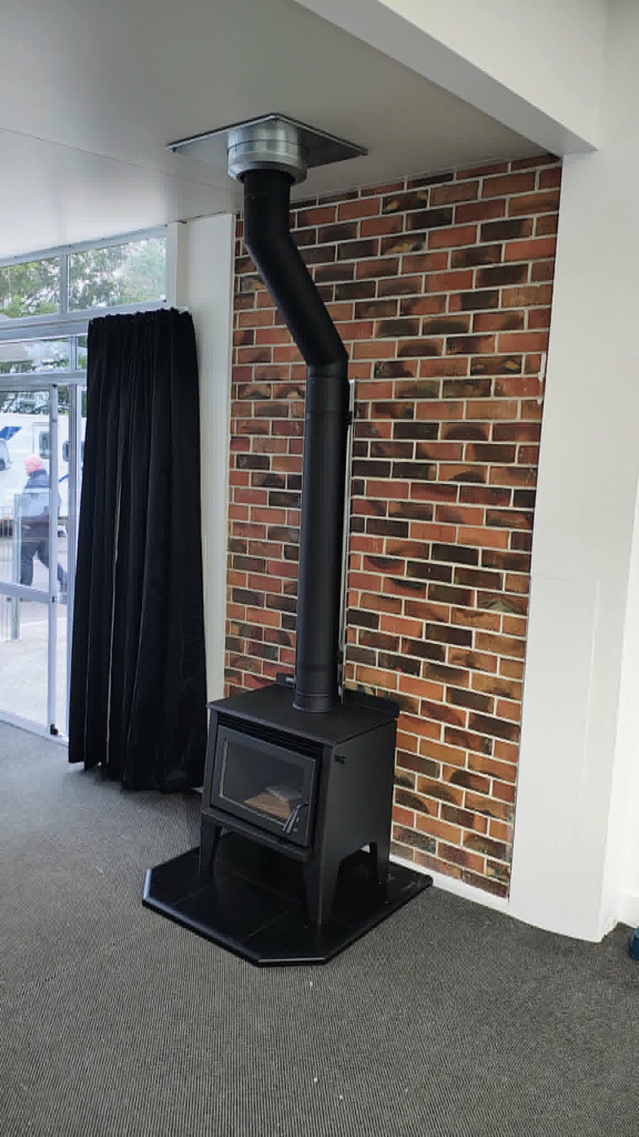 A sleek black freestanding wood fire against a brick feature wall, installed by Premium Fires