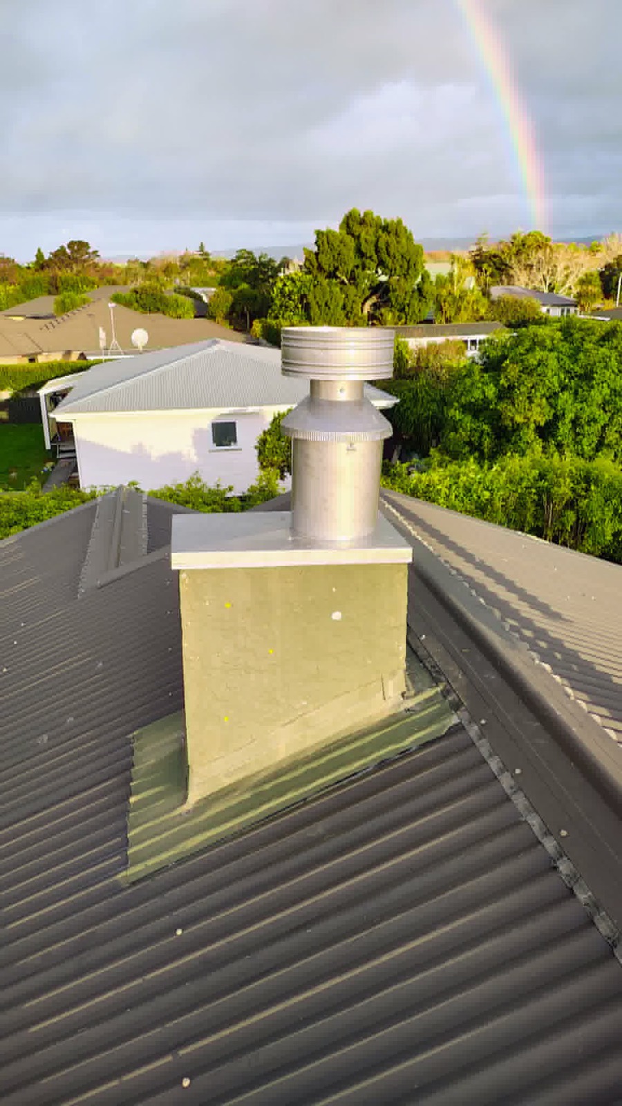 A new stainless steel flue and rain cap installed on a Northland metal roof, rainbow in the sky