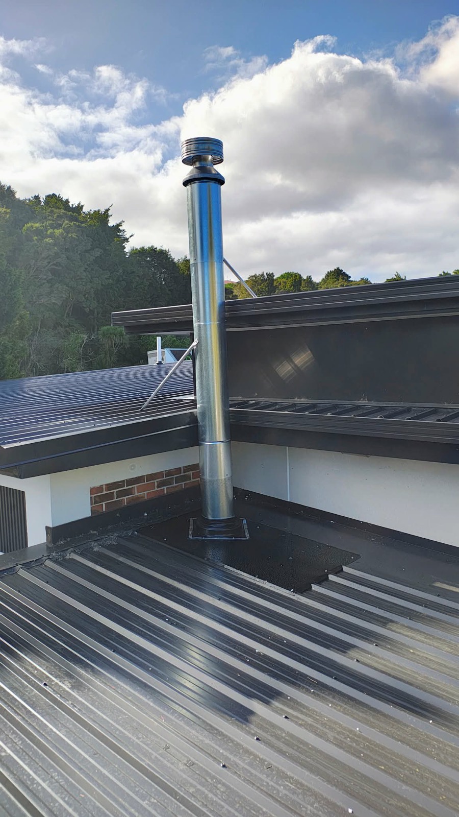 Galvanised flue penetrating a dark metal roof, flashed and sealed